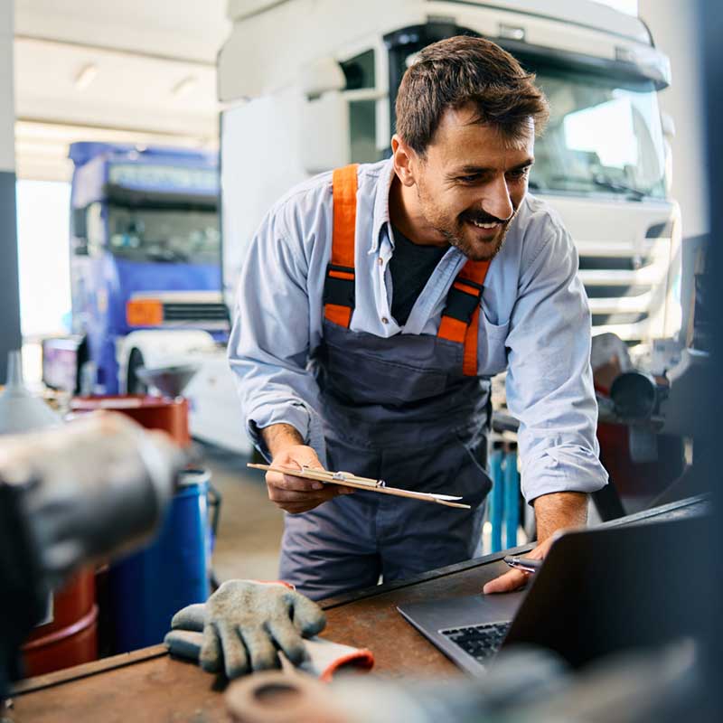 mechanic using laptop while working at truck repair workshop